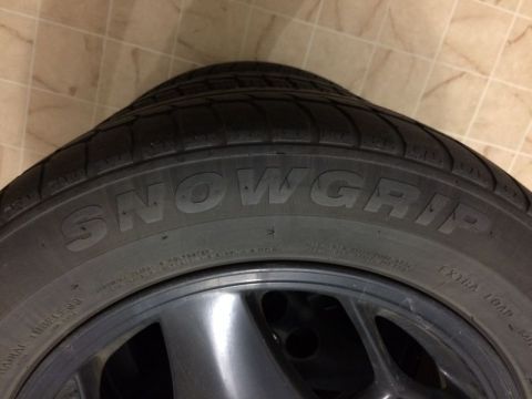 2002 Pontiac Grand Prix - A close-up, angled view of a tire with the "SNOWGRIP" brand name prominently displayed. The tire is mounted on a dark gray wheel, and the b…