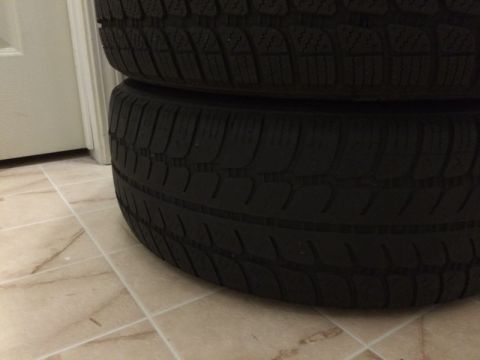2002 Pontiac Grand Prix - Two stacked tires are shown from a low angle, resting on a tiled floor next to a white door. The tires have a deep tread pattern.