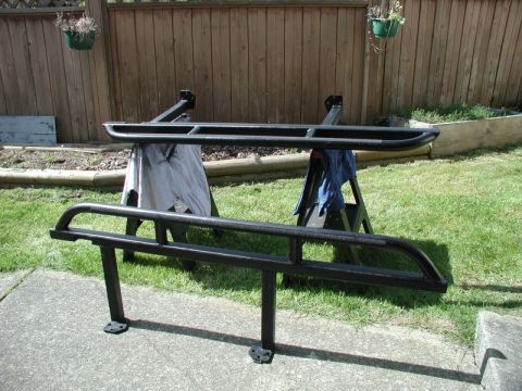 2002 Pontiac Grand Prix - Two black metal side steps are displayed outdoors, one resting on sawhorses and the other on the ground in front of a wooden fence.