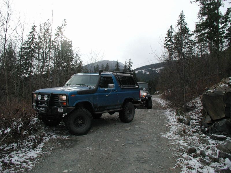 Blue SUV and dark Jeep on a snowy gravel road in a forest.