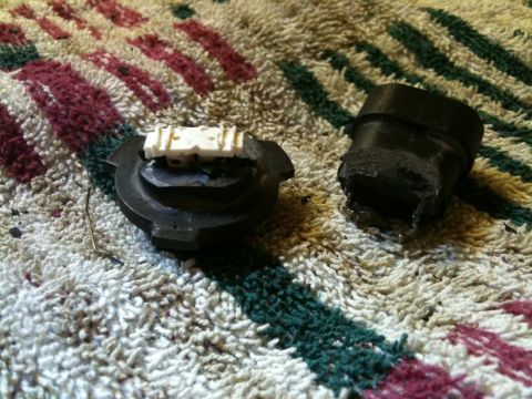2002 Pontiac Grand Prix - Two damaged black plastic automotive parts are shown on a textured rug. One part is a base with a white electrical connector, and the other…