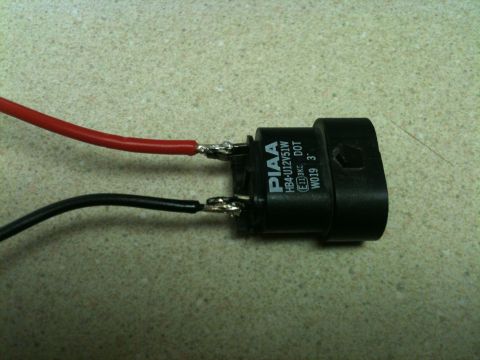 2002 Pontiac Grand Prix - A black PIAA HB4-U12V51W headlight bulb connector with red and black wires attached. The connector has text that reads "PIAA HB4-U12V51W E1…