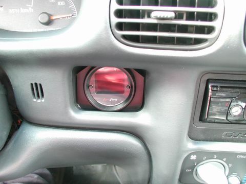 2002 Pontiac Grand Prix - A close-up view of a car's dashboard showing an aftermarket gauge installed in the center console, next to the air vents and a car stereo.
