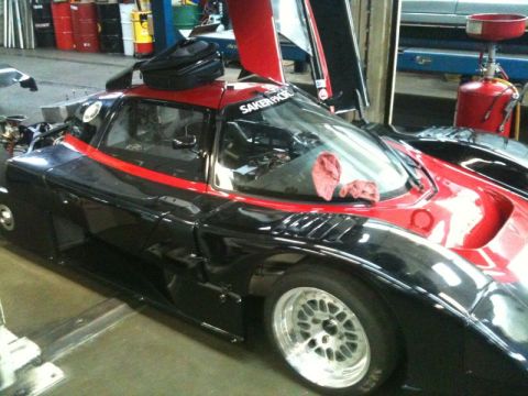 2002 Pontiac Grand Prix - A black and red race car is parked in a garage with its doors open. A black bag is placed on the roof of the car.
