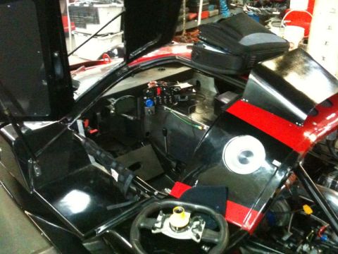 2002 Pontiac Grand Prix - The interior and engine bay of a black race car with red stripes are visible, with the doors and hood open. The steering wheel and dashboar…