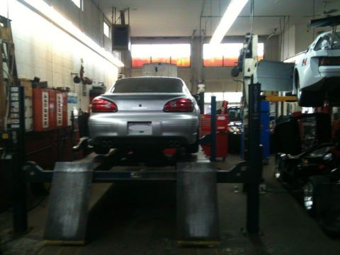 2002 Pontiac Grand Prix - A silver Pontiac Grand Prix is raised on a car lift in a repair shop. The rear of the car is visible, showing its taillights and dual exhau…