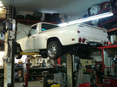 2002 Pontiac Grand Prix - A white pickup truck is raised on a hydraulic lift in a garage. The hood is open, revealing the engine bay, and the truck is viewed from th…