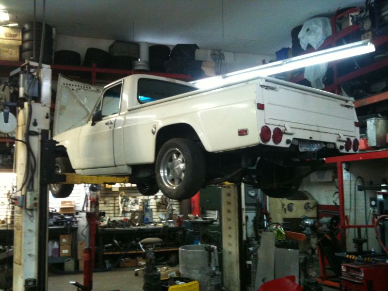 White pickup truck on a hydraulic lift in a garage, hood open.