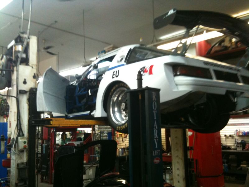 White race car on a lift with door open, showing roll cage.