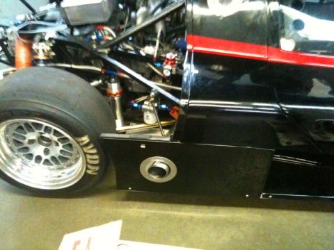 2002 Pontiac Grand Prix - Close-up side view of a black racing car with a red stripe on the body. The front tire and part of the engine bay are visible.