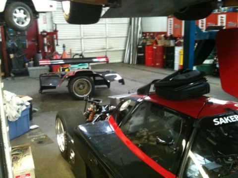 2002 Pontiac Grand Prix - A black and red sports car is parked in a garage with a trailer in the background. The car has a large black bag on its roof and the word "…
