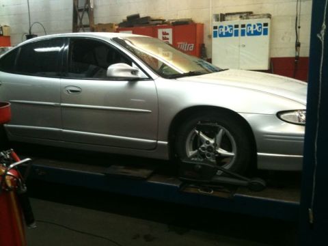 2002 Pontiac Grand Prix - A silver four-door sedan is parked on a vehicle lift in an auto repair shop. A wheel alignment machine is attached to the front passenger-s…