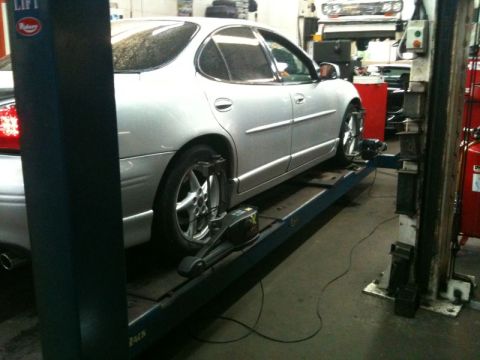 2002 Pontiac Grand Prix - A silver sedan is positioned on a car lift in a repair shop, with wheel alignment equipment attached to the front wheel. The vehicle is vie…