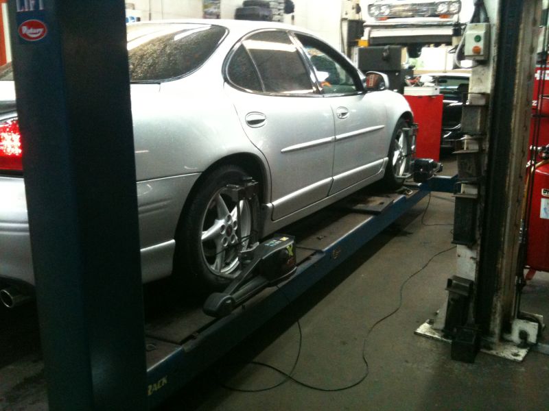 Silver sedan on a car lift with wheel alignment equipment attached.