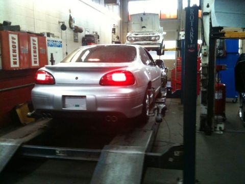 2002 Pontiac Grand Prix - The rear of a silver Pontiac Grand Prix is shown on a car lift in a garage. The car's taillights are illuminated, and it has dual exhaust p…