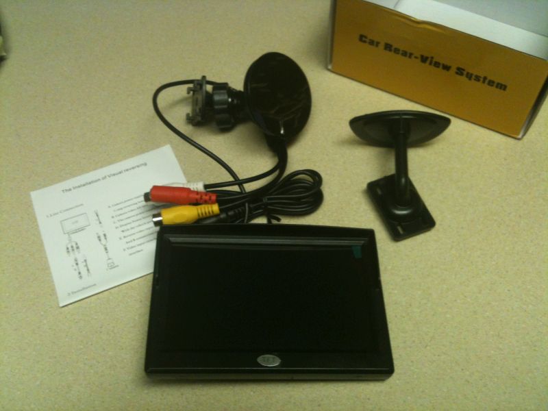 Car rear-view system kit with screen, camera, cables, mounts, and manual.