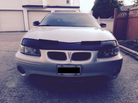 2002 Pontiac Grand Prix - Front view of a silver Pontiac Grand Prix with a black car bra covering the hood. The car is parked in a driveway in front of a white garag…