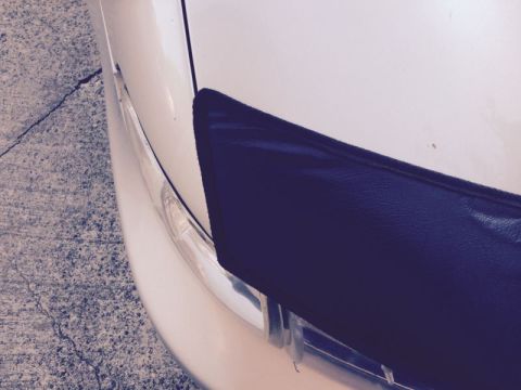 2002 Pontiac Grand Prix - A close-up, angled view of the front corner of a white car, showing a portion of the bumper and a dark-colored accessory attached to it. Th…
