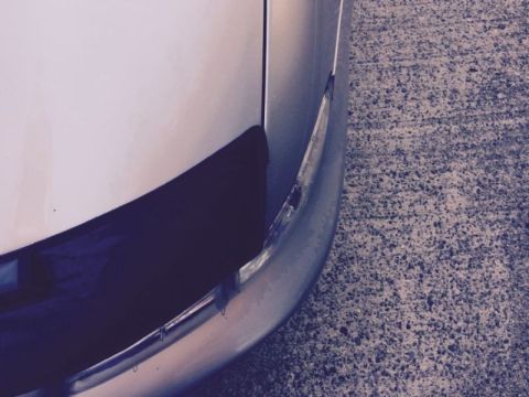 2002 Pontiac Grand Prix - A close-up, low-angle view of the front corner of a silver car, showing part of the bumper and a dark trim piece. The car is parked on a te…