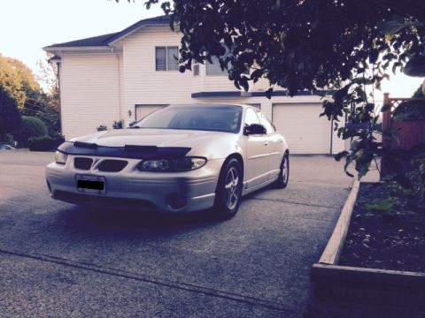 2002 Pontiac Grand Prix - A silver Pontiac Grand Prix is parked in a driveway in front of a white house with a two-car garage. The car has a black car bra on the fro…