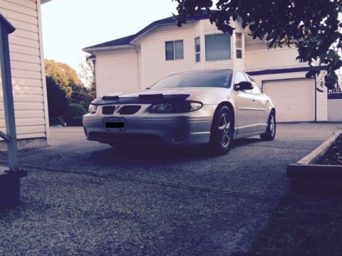 2002 Pontiac Grand Prix - A silver Pontiac Grand Prix is parked in a driveway in front of a white house and garage. The car has a black bug deflector on the hood and…