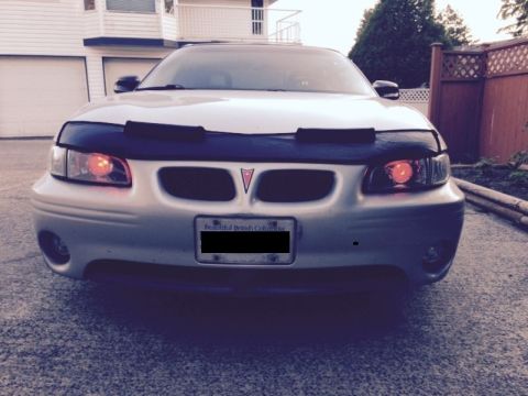 2002 Pontiac Grand Prix - Front view of a silver Pontiac Grand Prix with a black car bra and custom orange headlights. The car is parked in a driveway in front of a…