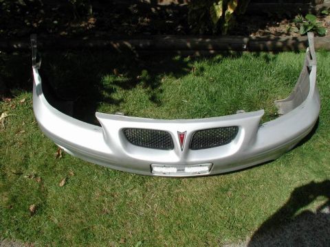 2002 Pontiac Grand Prix - A silver Pontiac Grand Prix front bumper cover is displayed outdoors on a grassy lawn. The bumper has a black mesh grille with a red Pontia…