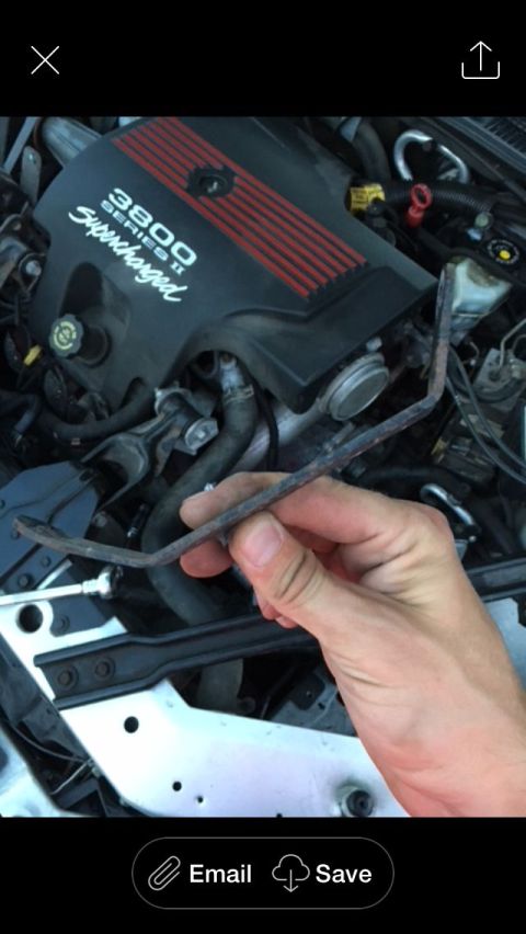 2002 Pontiac Grand Prix - A hand holds a bent metal bracket in front of a 3800 Series II Supercharged engine. The engine cover is black with red stripes and text.
