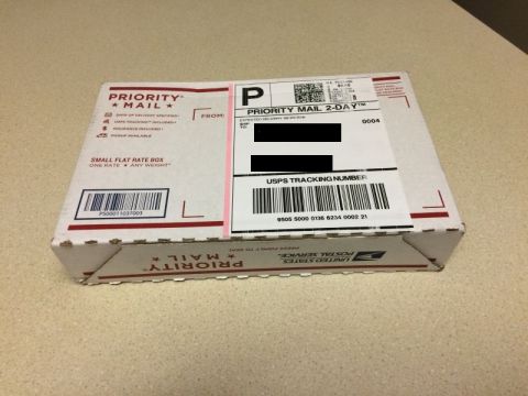 2002 Pontiac Grand Prix - A white USPS Priority Mail small flat rate box sits on a speckled surface. The box has shipping labels and barcodes visible.