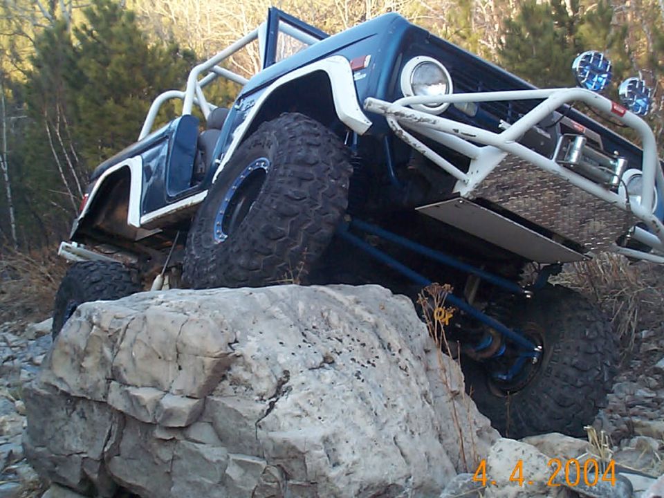 Blue caged Ford Bronco perched on a boulder, low angle showing suspension and winch bumper