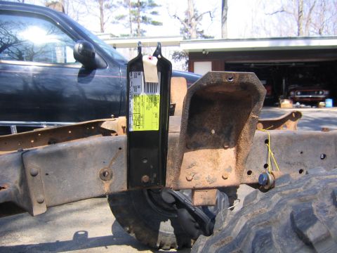 1978 Ford Bronco - New black shock-mount bracket with a yellow Ford parts barcode label still attached, hung on a stripped, rust-brown frame rail next to the…