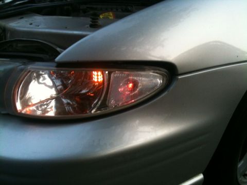 2002 Pontiac Grand Prix - Close-up of the front passenger-side headlight assembly of a silver car, showing the turn signal with amber LEDs and the brake light with a…