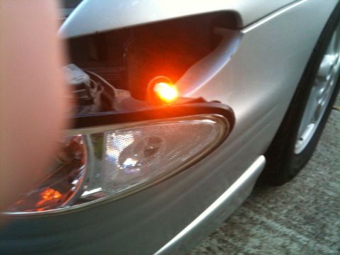 2002 Pontiac Grand Prix - A close-up, low-angle shot of the front passenger side of a silver sedan. The amber turn signal light is illuminated, and the headlight ass…