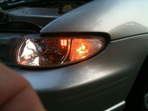 2002 Pontiac Grand Prix - A close-up view of the front passenger side headlight assembly of a silver car. The headlight features an orange turn signal with a grid of…
