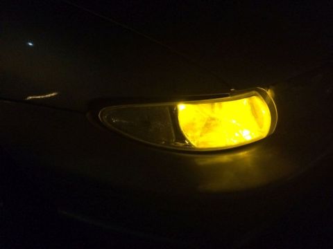 2002 Pontiac Grand Prix - A close-up, low-angle shot of a yellow fog light on the front of a dark-colored vehicle at night. The light illuminates the surrounding dar…