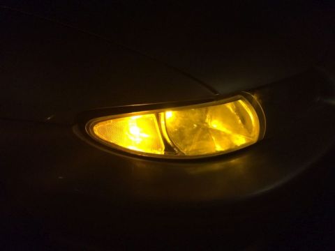 2002 Pontiac Grand Prix - A close-up of a yellow headlight on a dark colored vehicle. The headlight has a textured lens on the left and a faceted lens on the right.
