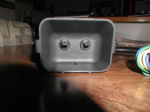 2002 Pontiac Grand Prix - A gray plastic housing with two circular openings is shown from the front, resting on a wooden surface. A bundle of colored wires emerges f…