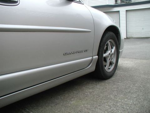 2002 Pontiac Grand Prix - A close-up side view of a silver Pontiac Grand Prix GT shows the lower body paneling and the front wheel. The car is parked on a concrete d…