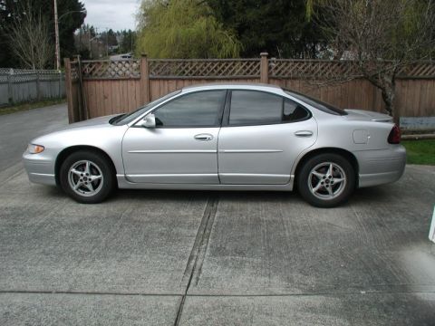 2002 Pontiac Grand Prix - The side view of a silver 2002 Pontiac Grand Prix sedan is parked on a concrete driveway. The car has tinted windows and is positioned in f…
