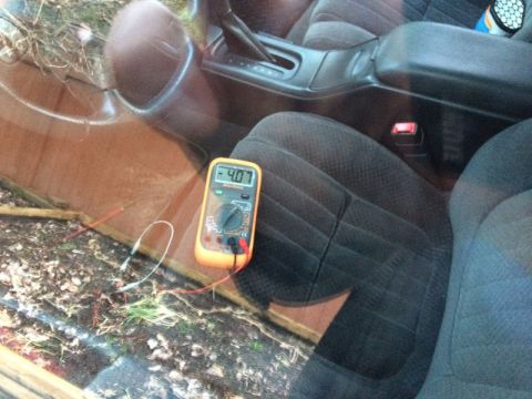 2002 Pontiac Grand Prix - An orange digital multimeter with a reading of 4.07 is placed on the ground next to the interior of a car. The multimeter's probes are conn…