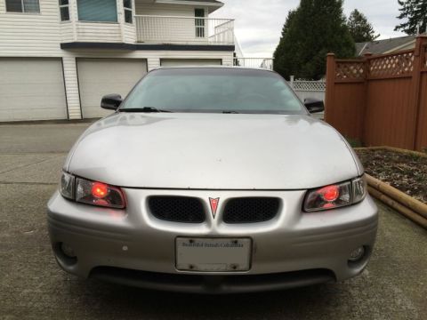2002 Pontiac Grand Prix - Front view of a silver Pontiac Grand Prix with custom red halo headlights. The car is parked in a driveway in front of a house with a woode…