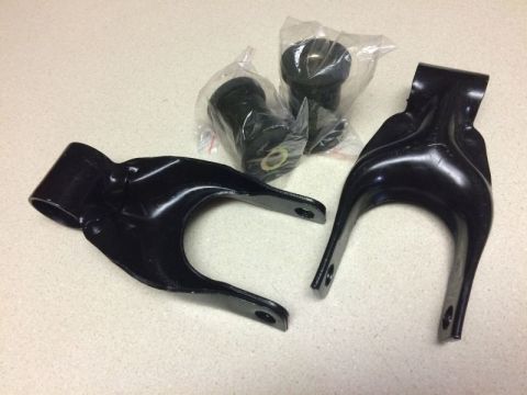 2002 Pontiac Grand Prix - Two black metal suspension control arms and two black rubber bushings in plastic packaging are laid out on a speckled countertop.