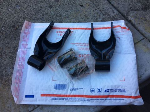 2002 Pontiac Grand Prix - Two black metal suspension components with a U-shaped yoke and a cylindrical base are laid out on a white USPS Priority Mail padded envelop…