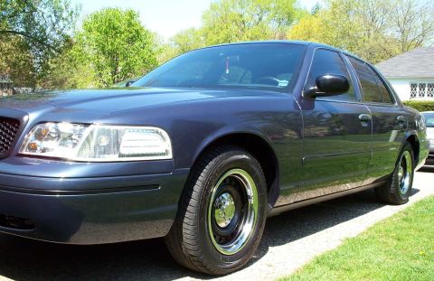 1998 Ford Crown Victoria - A dark blue sedan is parked on a sunny day, with trees and a house in the background.