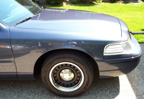 1998 Ford Crown Victoria - Front driver's side fender and wheel of a dark blue 1998 Ford Crown Victoria, steel wheels with chrome hubcaps.