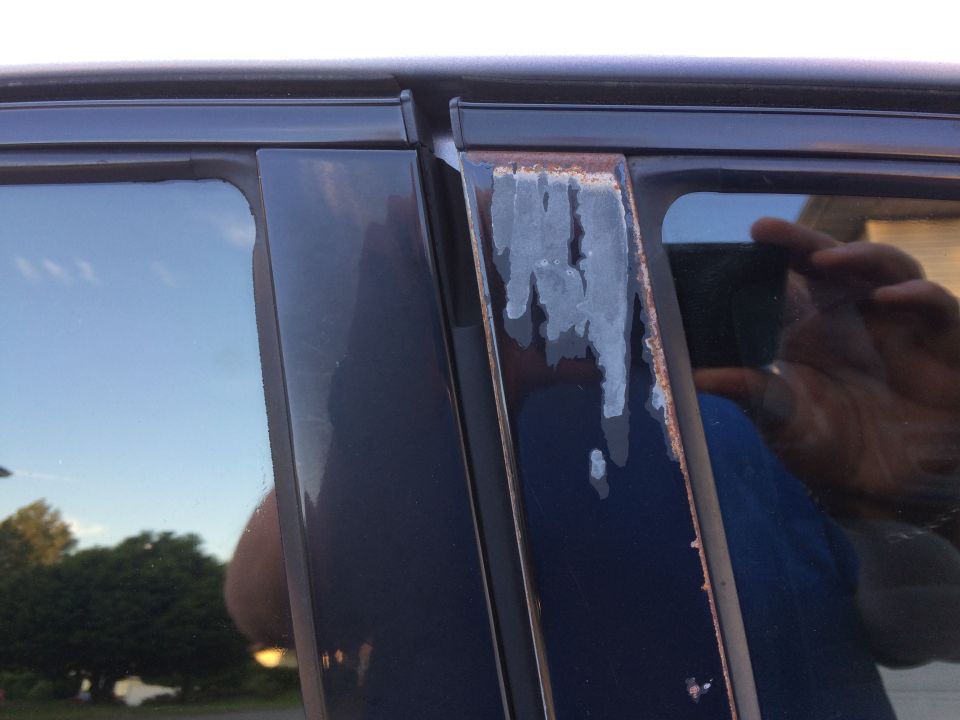 Close-up of rusty B-pillar on a dark blue car.