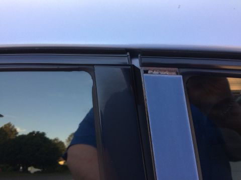 2002 Pontiac Grand Prix - Close-up view of the upper corner of a car door window frame, showing rust on the metal trim piece next to the window. The sky and trees ar…