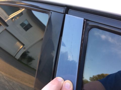 2002 Pontiac Grand Prix - A person's hand is shown holding a gray trim piece that is detached from the driver's side door frame of a dark-colored vehicle. The trim p…