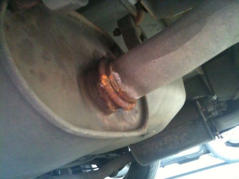 2002 Pontiac Grand Prix - The underside of a vehicle shows a rusted exhaust system, including a muffler and connecting pipe. The connection point between the pipe an…
