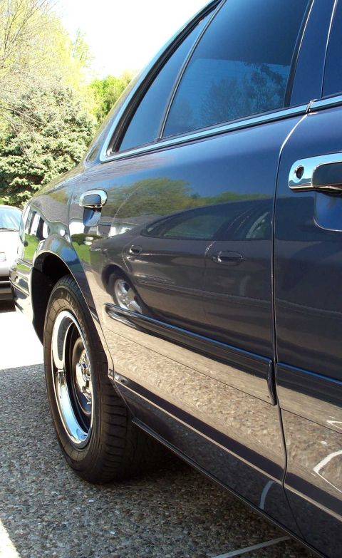 1998 Ford Crown Victoria - The side profile of a dark blue sedan is captured, highlighting its reflective paint and chrome accents.